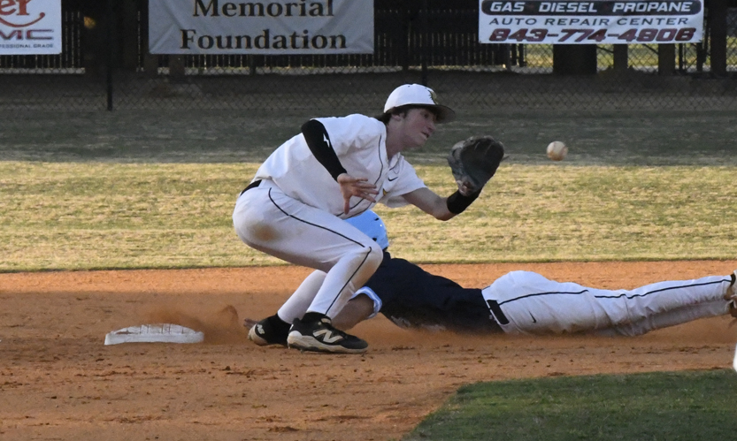 Baseball player in white attempts to tag out a sliding runner at second base as the ball approaches.