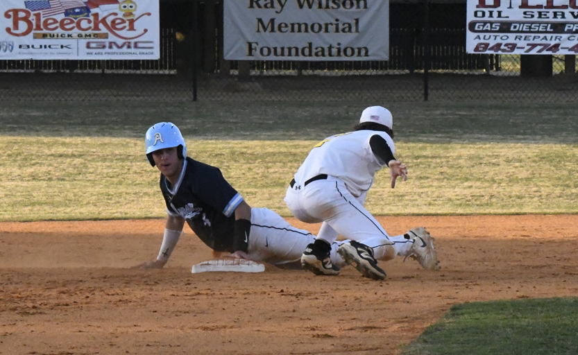 A baseball player in blue slides safely to a base as another player in white attempts to tag him out during a game.