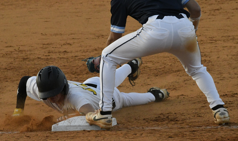 A baseball player slides headfirst into a base as another player attempts to tag them during a game on a dirt field.