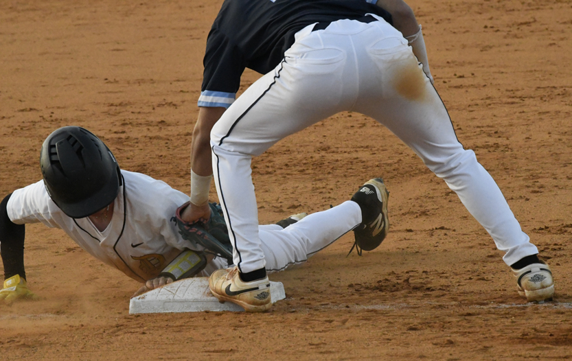 A baseball player slides into a base as another player attempts to tag them out on a dirt field.