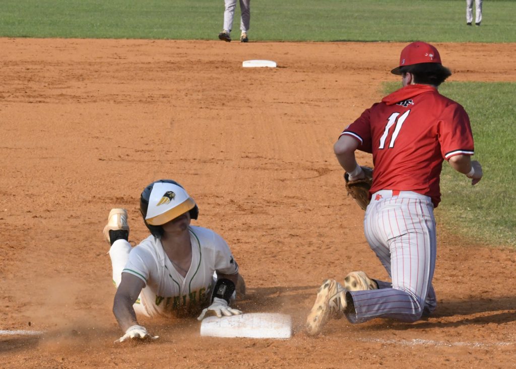 A baseball player in white slides into a base as an opponent in red attempts a tag on a dusty infield.