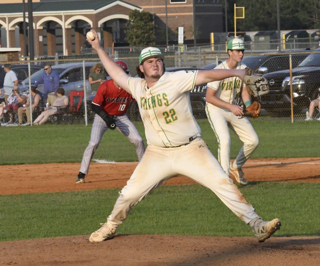 A baseball pitcher in a white "Vikings" uniform throws a pitch, with teammates and an opposing baserunner in the background.