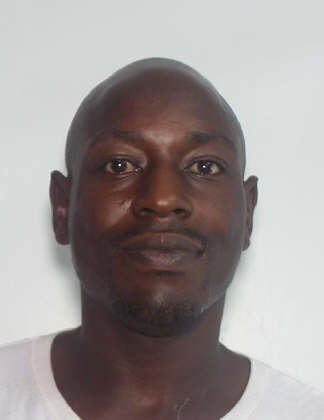 Portrait of a man with a shaved head, neutral expression, and wearing a white shirt against a plain background.