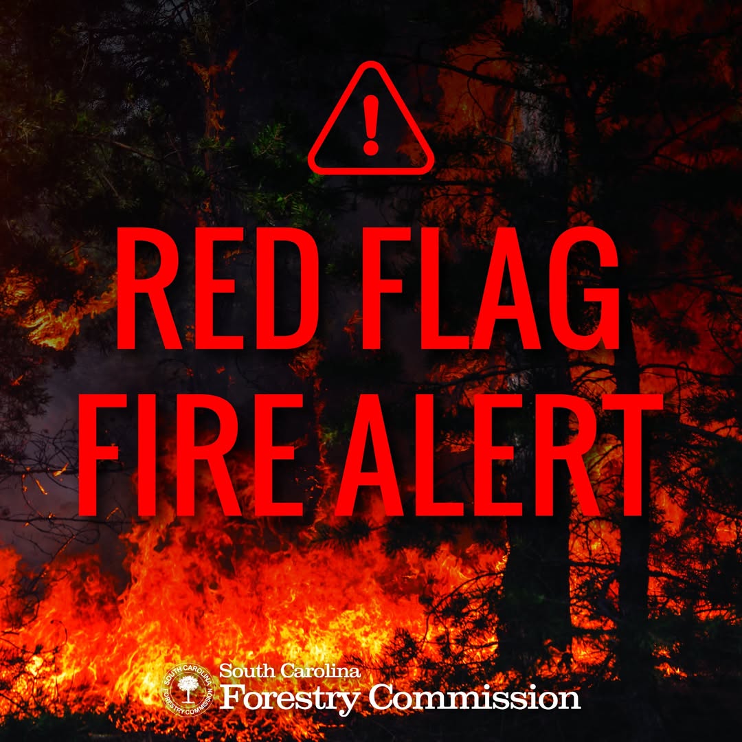 A forest fire with bold red text overlay reading “Red Flag Fire Alert” and a warning symbol, issued by the Forestry Commission.