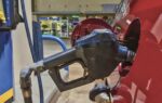 A black gasoline pump nozzle inserted into the fuel tank of a red vehicle at a gas station.