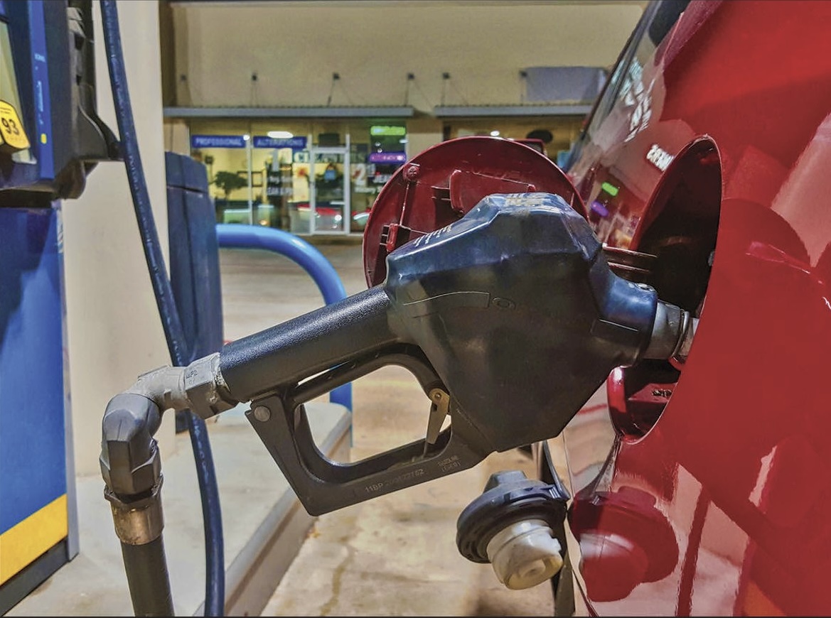 A black gasoline pump nozzle inserted into the fuel tank of a red vehicle at a gas station.