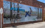 Mural on brick wall depicting trees, water, two flying birds, and text reading "Little Pee Dee River."