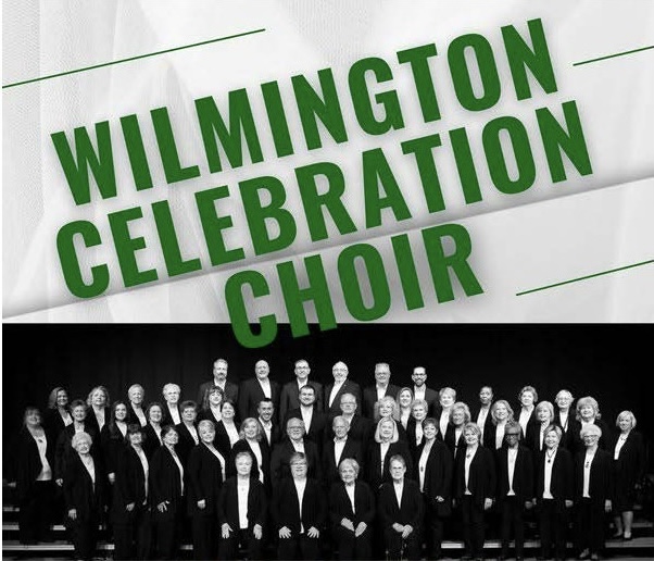 A large choir dressed in formal black attire stands together on stage under a sign reading "Wilmington Celebration Choir."