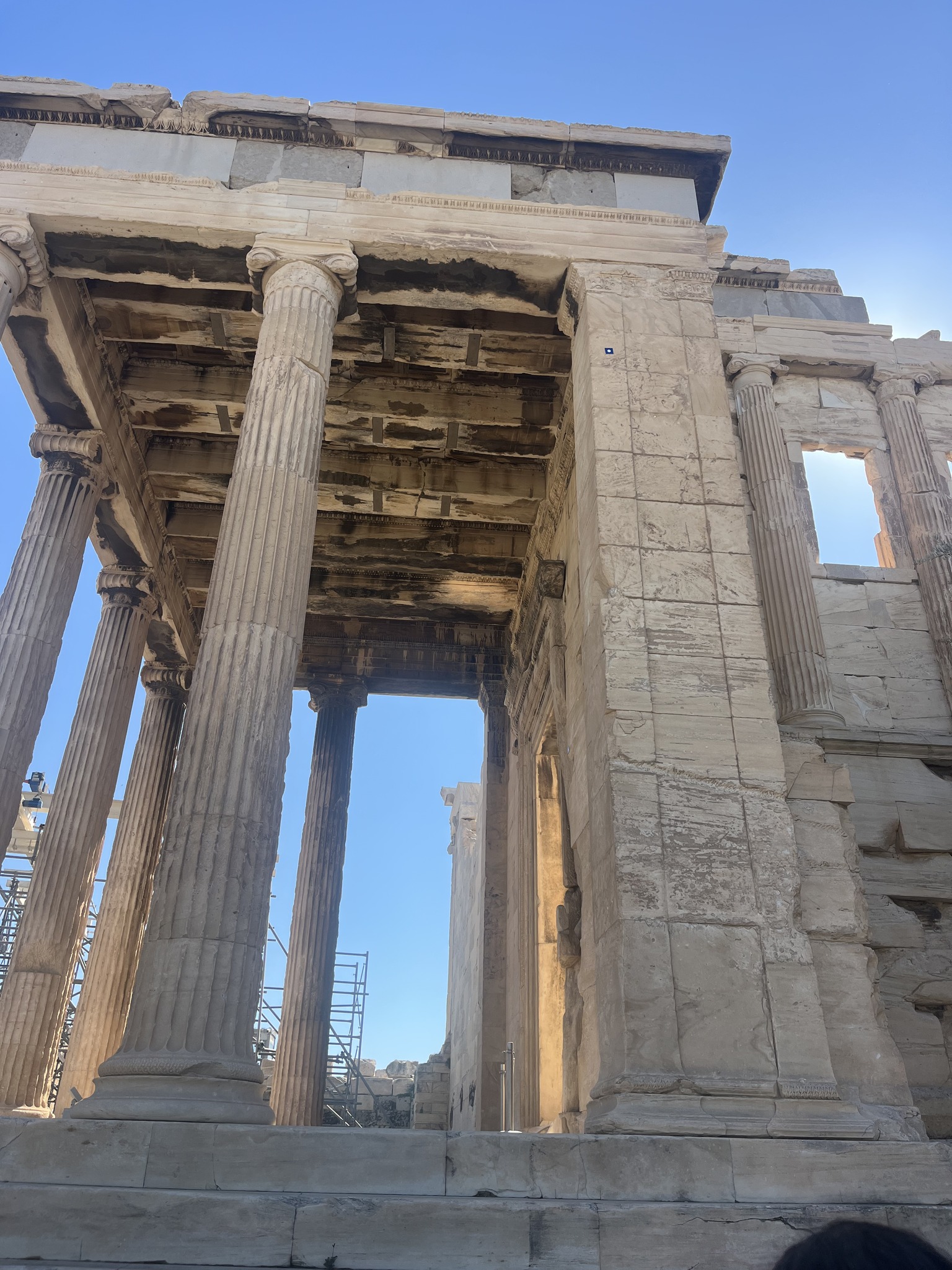 Ancient stone columns and ruins of a Greek temple, viewed from below, with clear blue sky in the background.