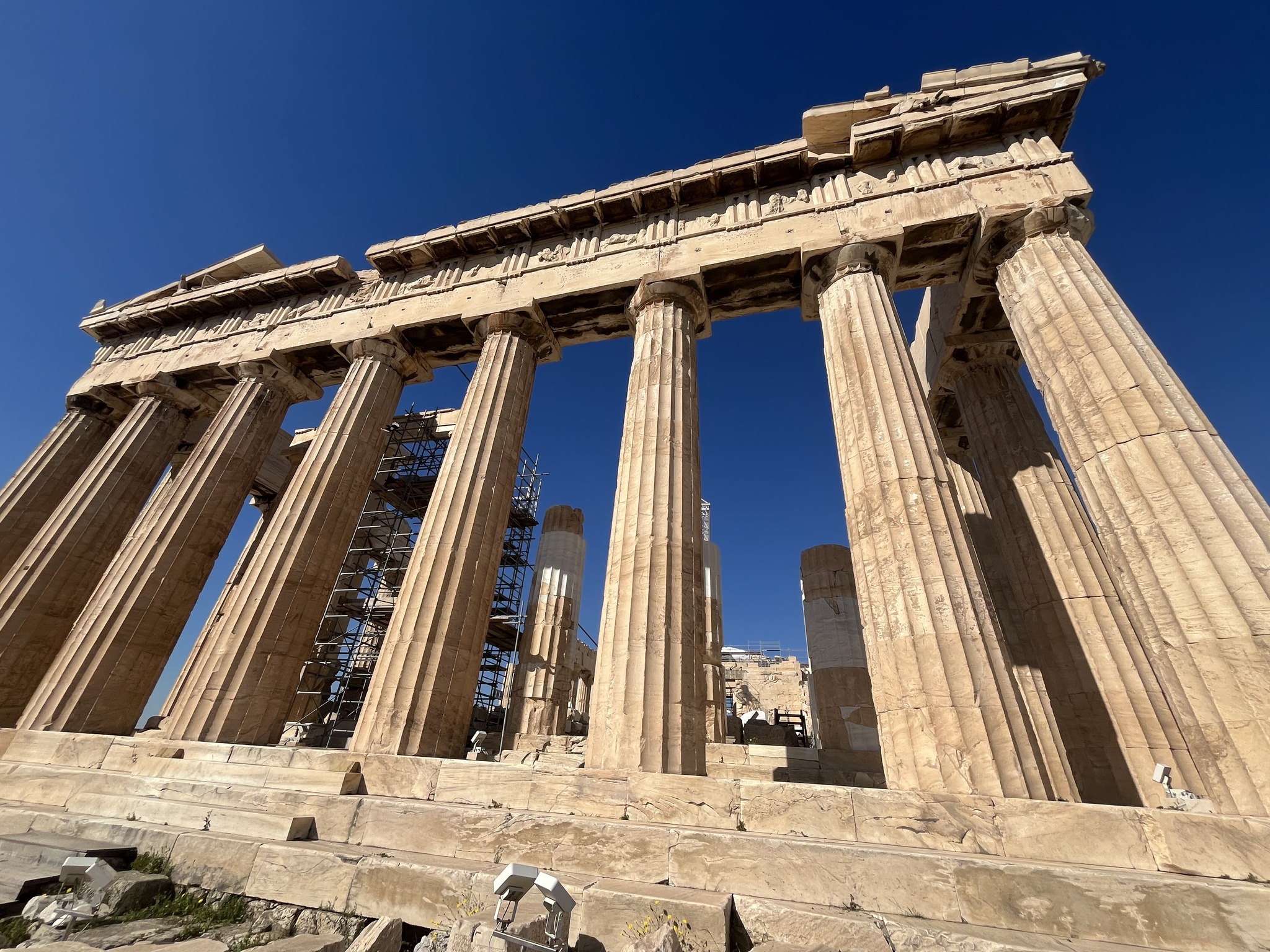 Ancient Greek temple with tall marble columns and blue sky background, part of the Parthenon ruins in Athens.