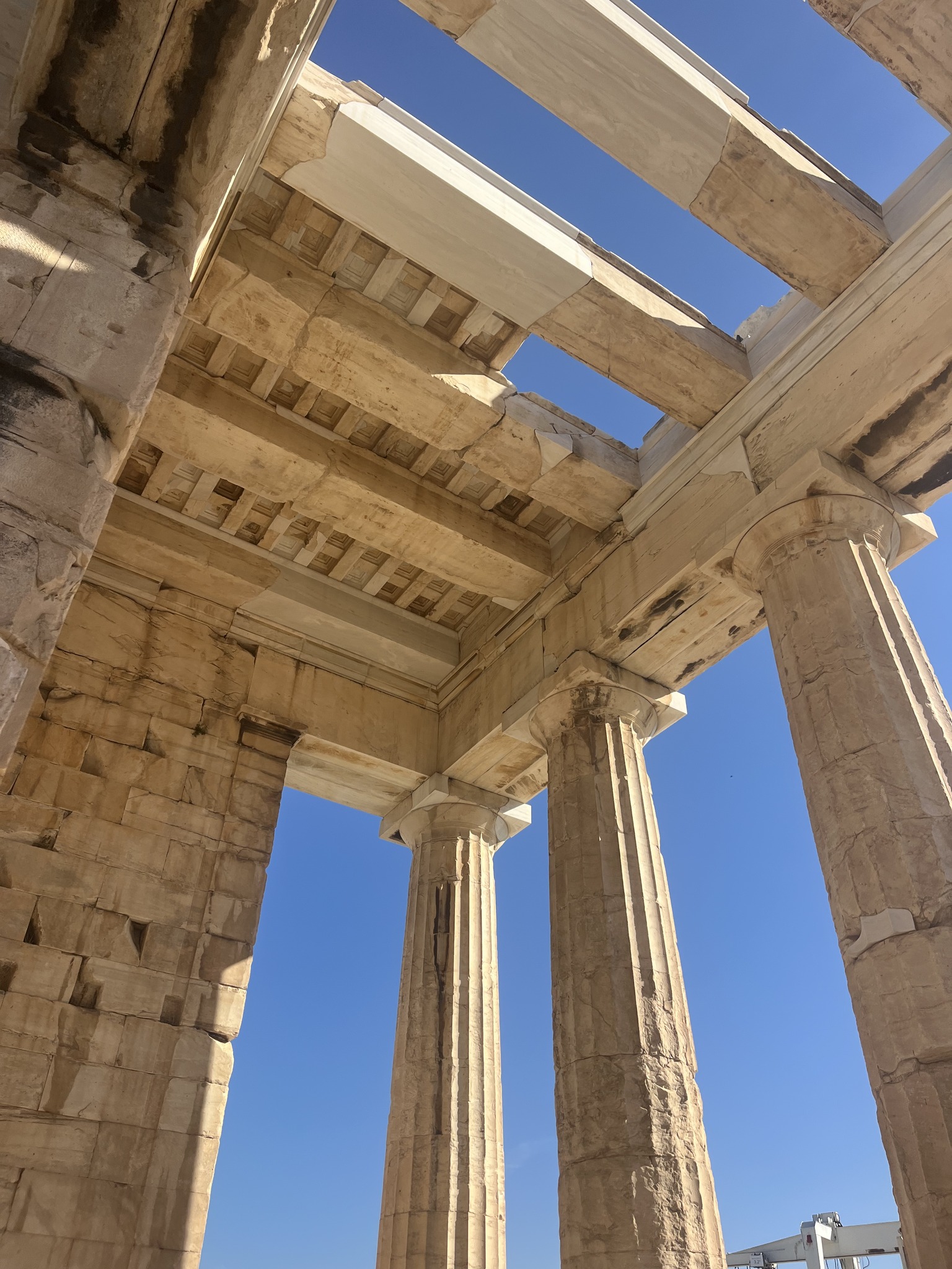 View from below of ancient stone columns and beams, part of a historic Greek temple, against a clear blue sky.