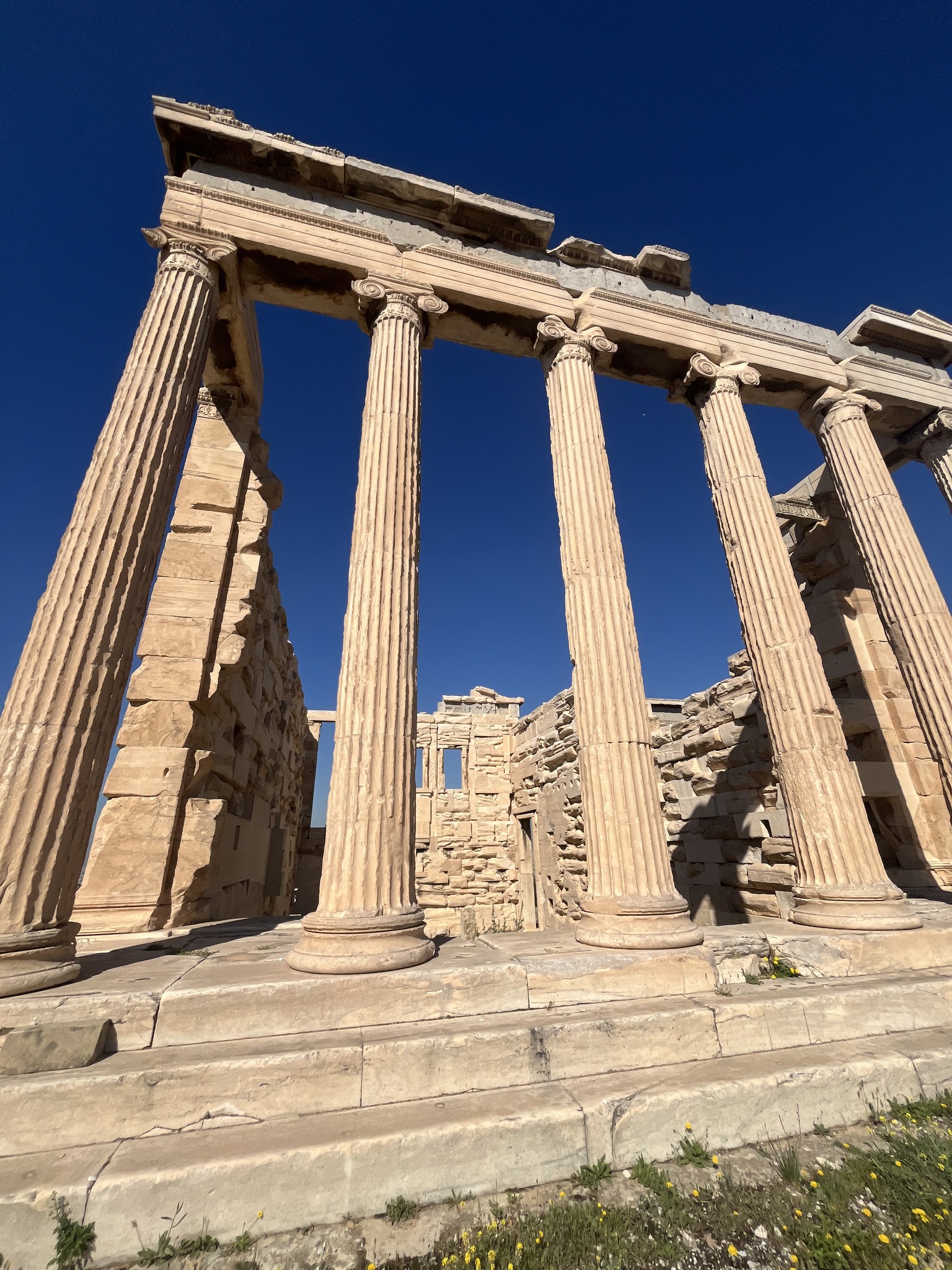 Ancient stone columns and ruins under a clear blue sky, resembling classical Greek architecture.