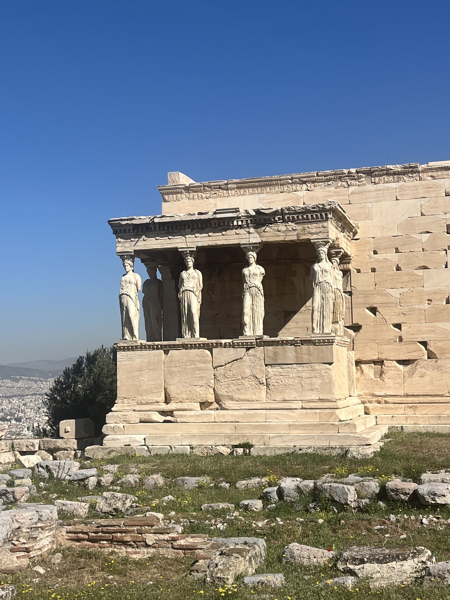 Ancient Greek temple with columns sculpted as women, known as caryatids, under a clear blue sky.