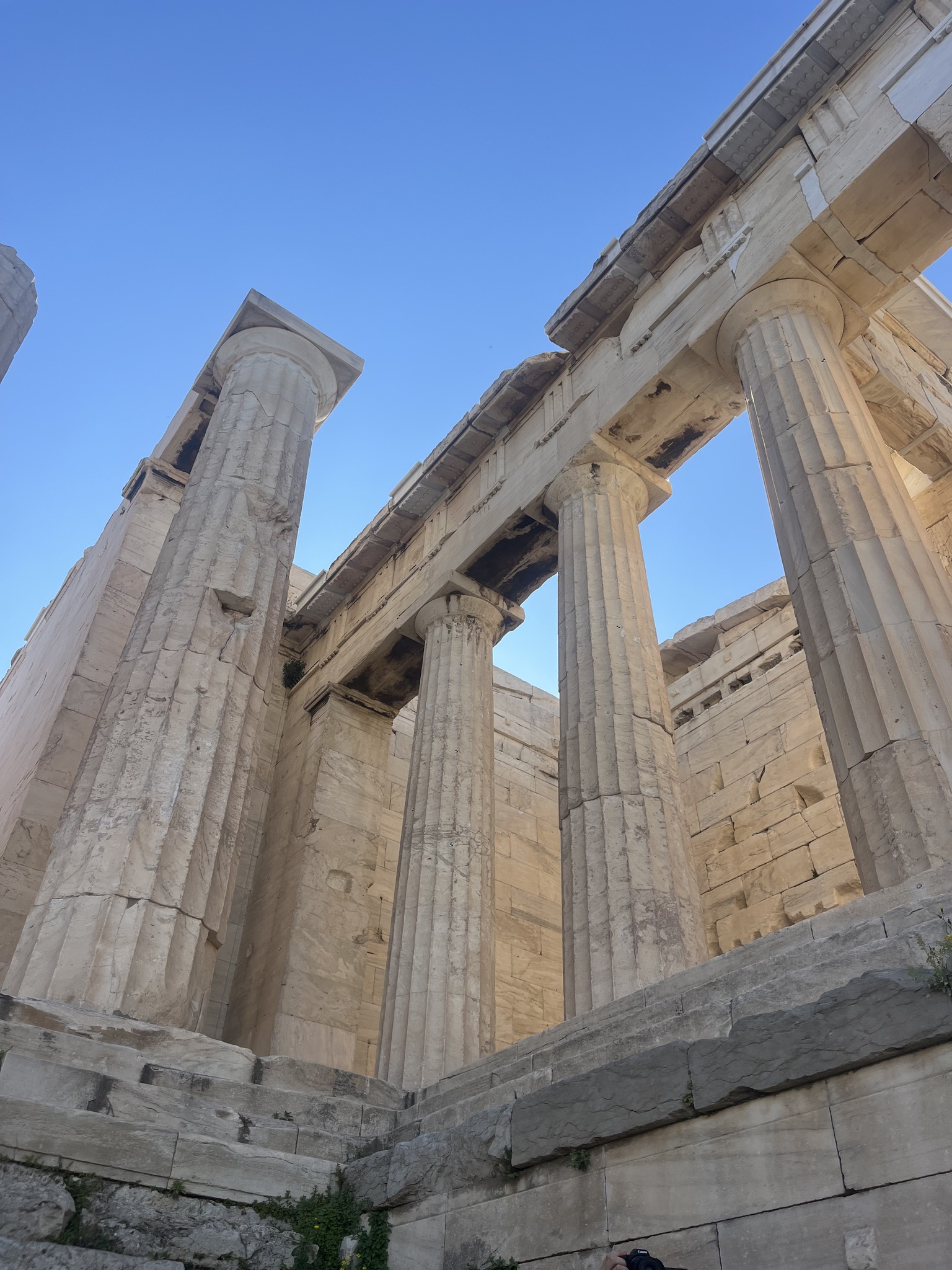 Ancient stone columns of a Greek temple, viewed from below against a clear blue sky.