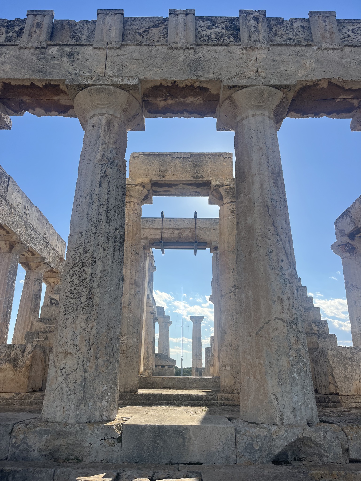 Ancient Greek temple ruins with tall stone columns and blue sky visible through the openings.