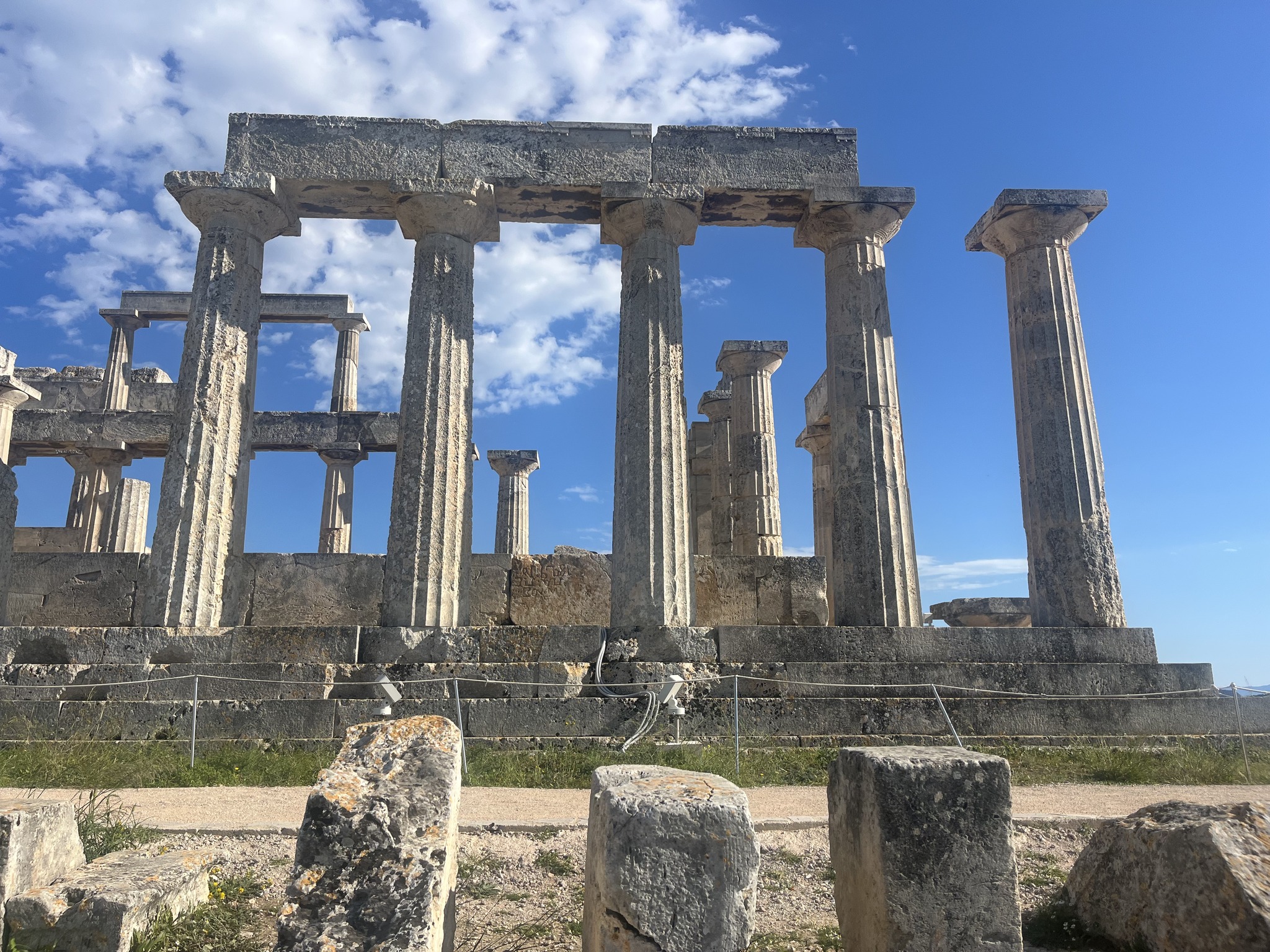 Ruins of an ancient Greek temple with tall stone columns, blue sky, and scattered clouds in the background.