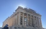 Ancient Greek Parthenon temple with columns and scaffolding under a clear blue sky, sunlight shining behind the structure.