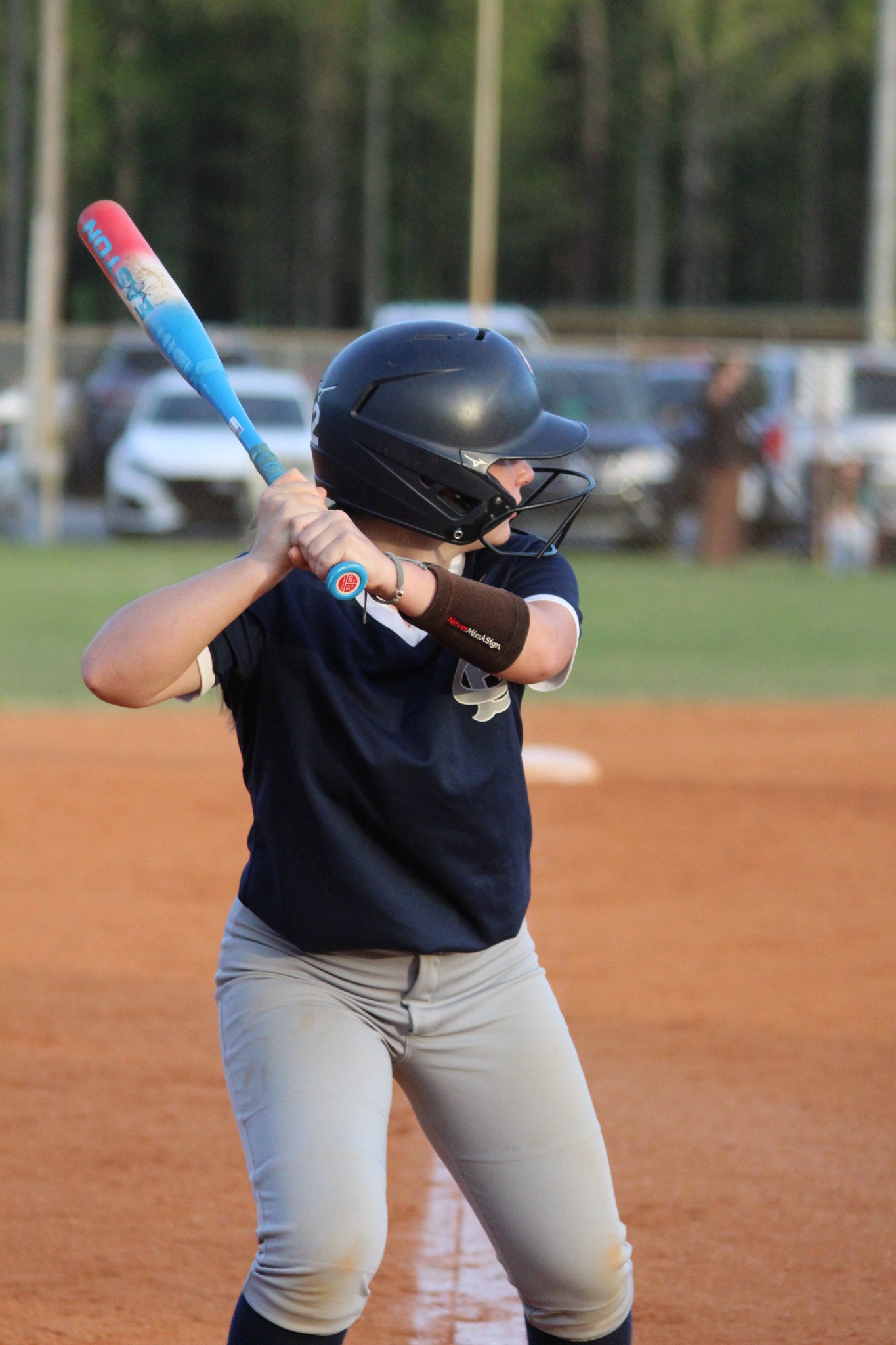 A baseball player wearing a helmet holds a bat, preparing to swing at home plate on a baseball field during a game.