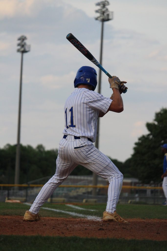 Baseball player in pinstripe uniform and helmet preparing to bat during a game, standing at home plate on an outdoor field.