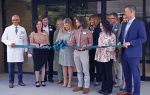 A group of people standing in front of a building, holding a large ribbon, participating in a ribbon-cutting ceremony.