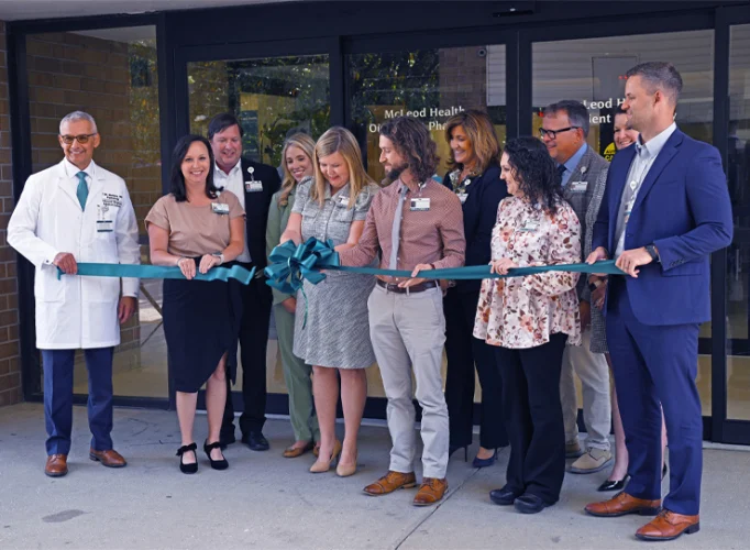 A group of people standing in front of a building, holding a large ribbon, participating in a ribbon-cutting ceremony.