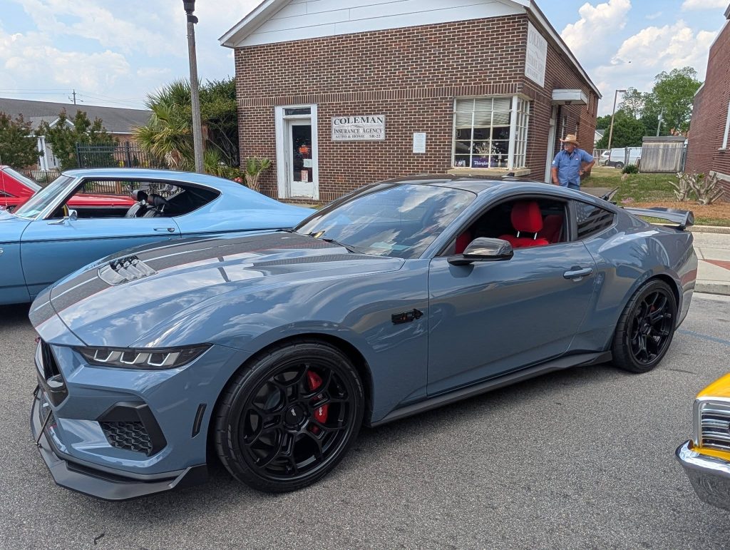 A grey sports car with black wheels and red accents parked on the street in front of a brick building.