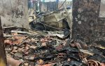 Burnt building with charred walls and debris, including broken tiles and metal, scattered on the ground; visible damage from a recent fire.