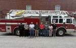 A group of people stands in front of a red and white Dillon County fire truck parked beside a brick building.