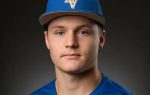 Young man wearing a blue baseball cap with "LV" letters and a matching blue shirt, looking directly at the camera with a neutral expression against a dark background.