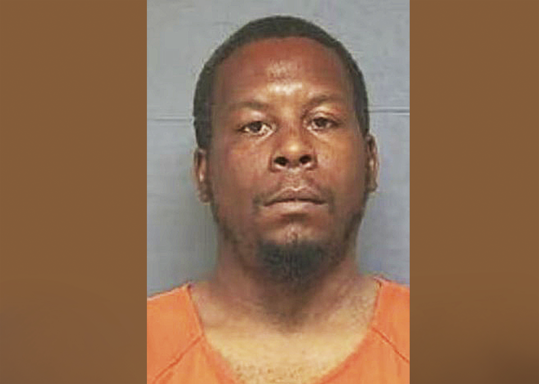 A man in an orange prison uniform facing the camera for a mugshot, with a neutral background.