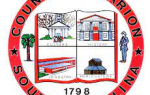 Seal of Marion County, South Carolina, featuring four quadrants with buildings, a tree, a person, and the year 1798, all within a red circular border.