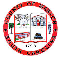 Seal of Marion County, South Carolina, featuring four quadrants with buildings, a tree, a person, and the year 1798, all within a red circular border.