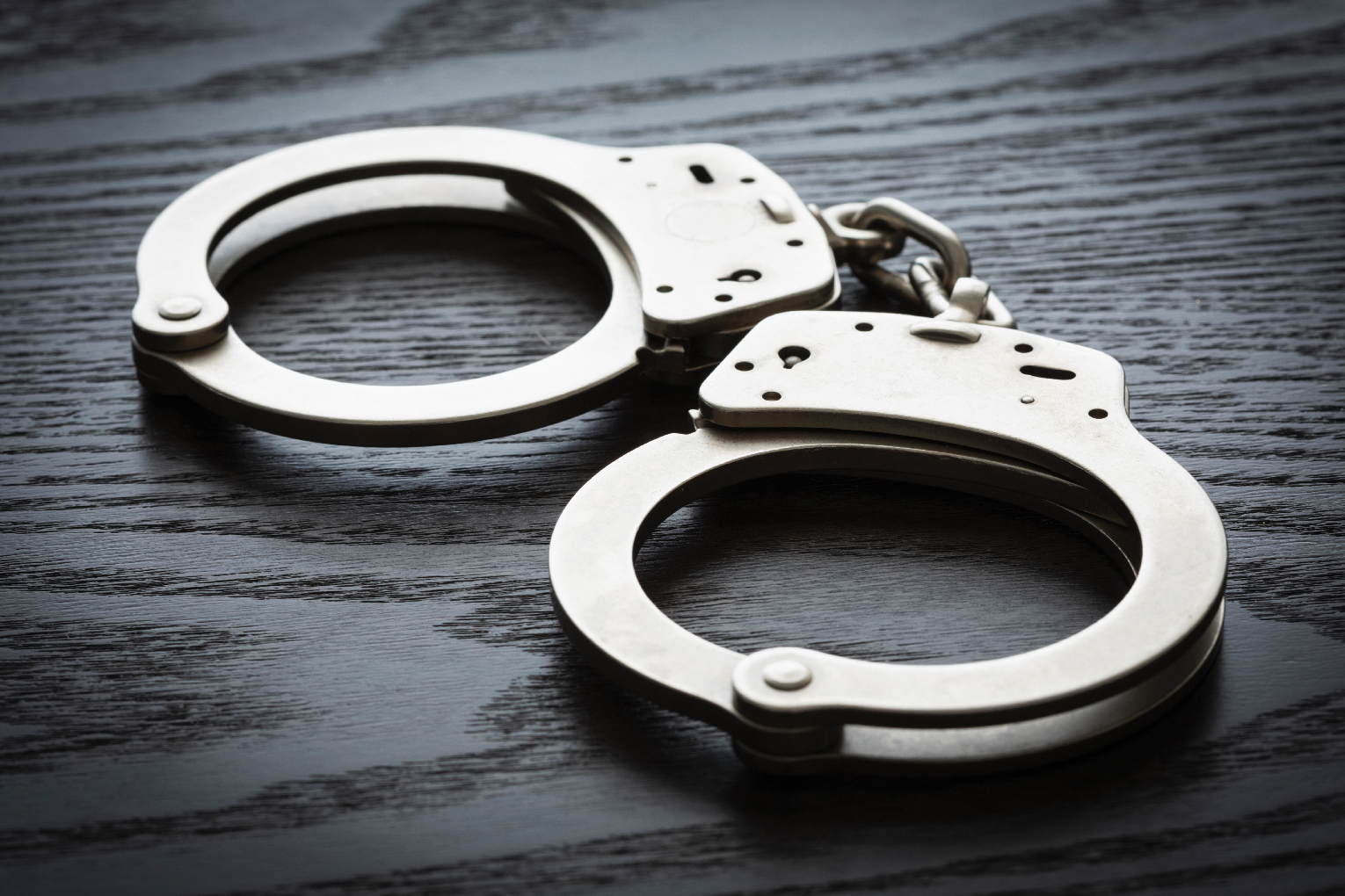 A pair of metal handcuffs lies unlocked on a dark wooden surface.