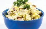 Potato salad with mayonnaise and chopped herbs served in a blue bowl, garnished with a sprig of parsley.