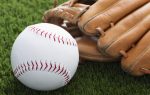 A baseball and a brown leather glove resting on green grass.