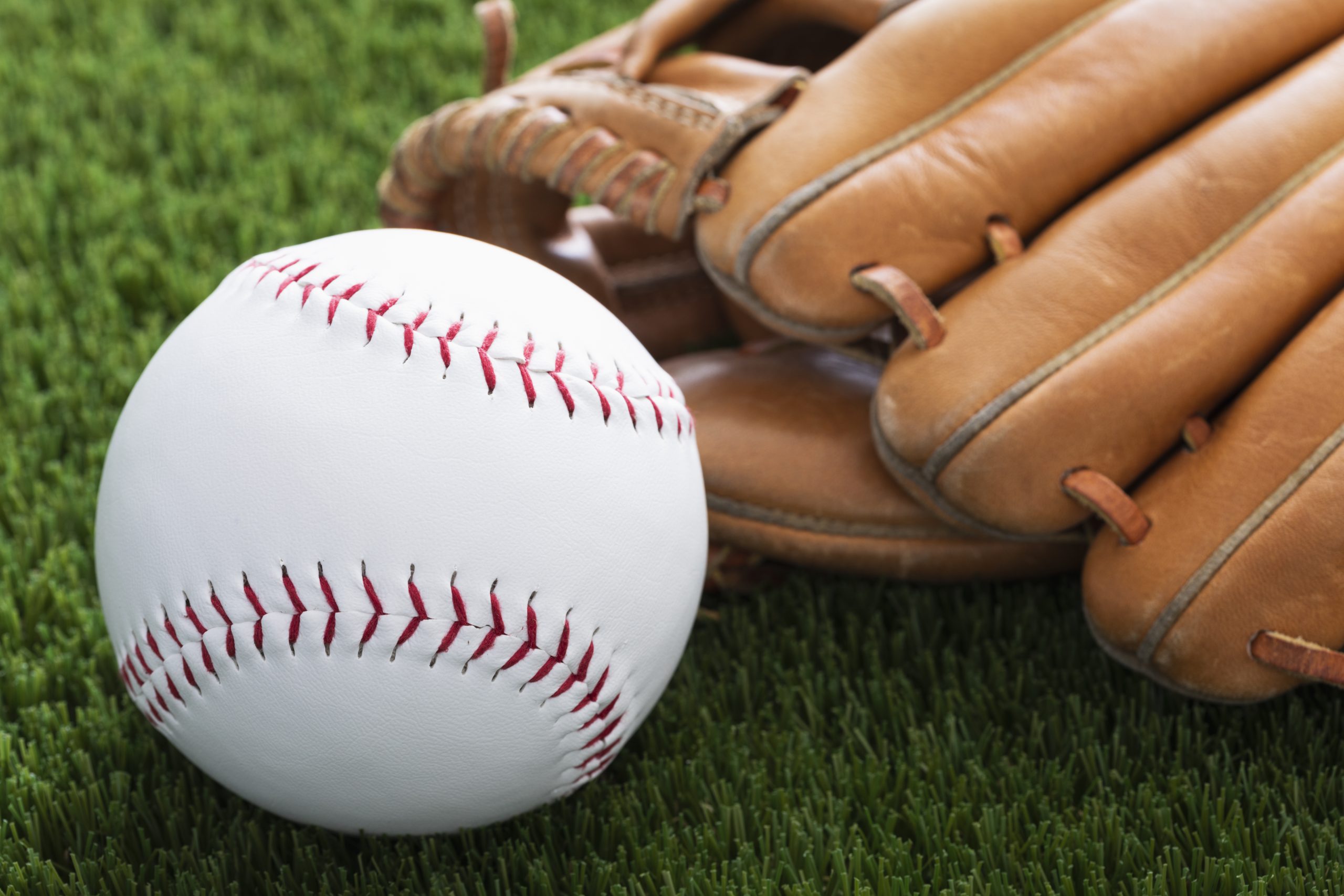 A baseball and a brown leather glove resting on green grass.