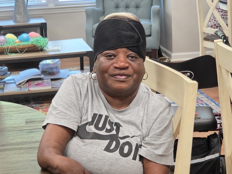 Woman wearing a black headband and gray "Just Do It" Nike t-shirt, sitting at a table in a cozy living room with pastel decor and magazines.