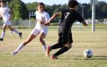 Two soccer players compete for the ball on a grassy field, with one in a white uniform and the other in black.