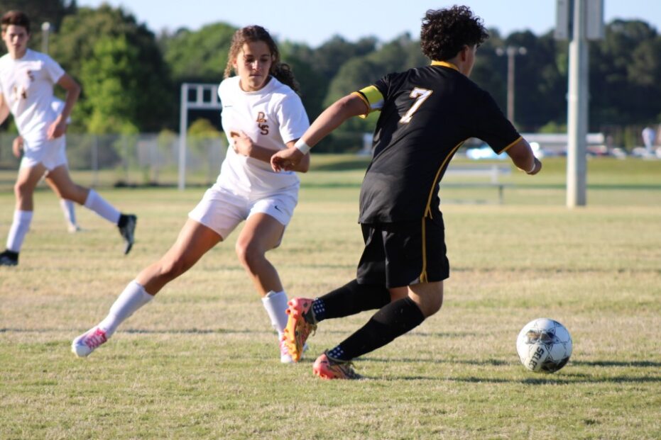 Two soccer players compete for the ball on a grassy field, with one in a white uniform and the other in black.