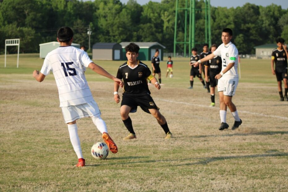 Boys playing a high school soccer match on a grassy field, with players in white and black uniforms competing for the ball.