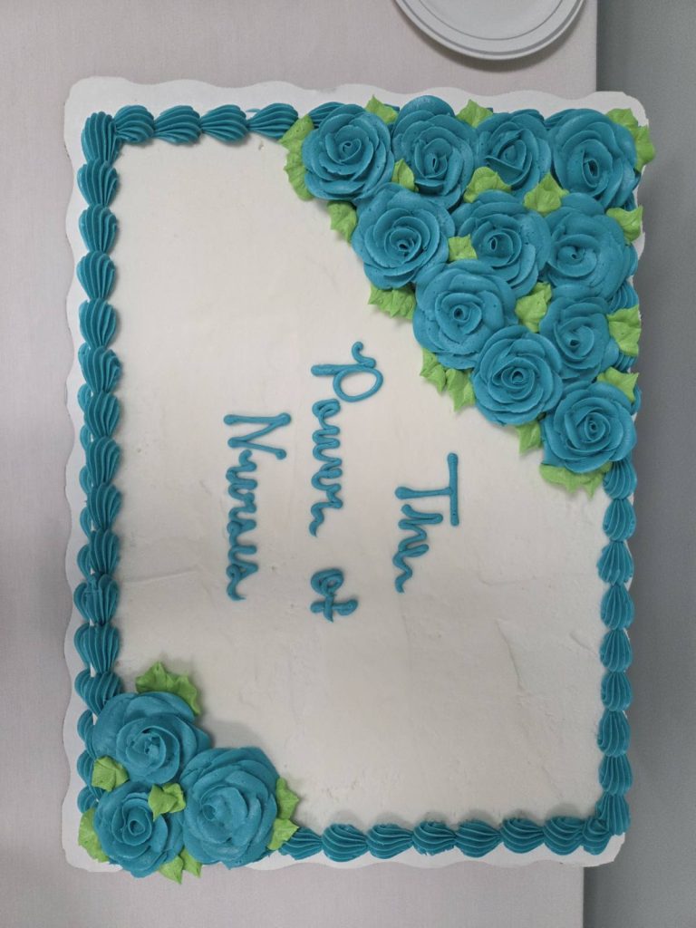 Rectangular cake with white icing, blue rose decorations, and the words "The Power of Nurses" written in blue icing.