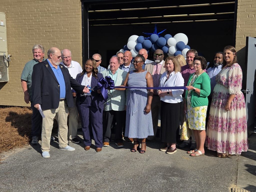 A group of people at a ribbon-cutting ceremony, standing in front of a building decorated with blue and white balloons.