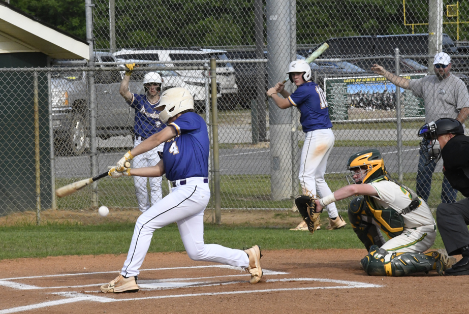 Baseball player in blue jersey swings bat and makes contact with ball, while catcher, umpire, and other players watch the action on a sunny day.