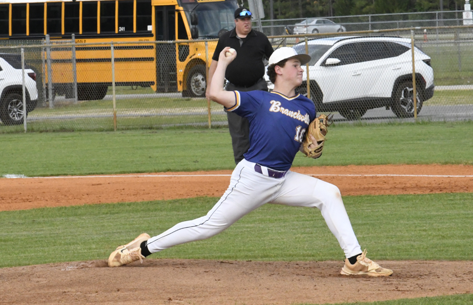 A baseball player in a blue jersey pitches on a field, an umpire and school bus are visible in the background.