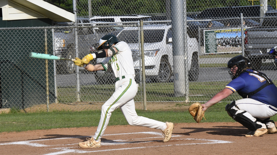 A baseball player swings at a pitch while a catcher crouches behind home plate during a daytime game.