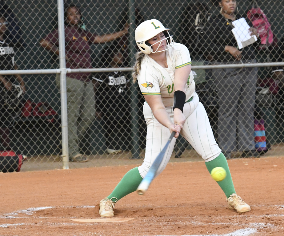 A softball player in a white uniform swings a bat and makes contact with a yellow softball during a game.