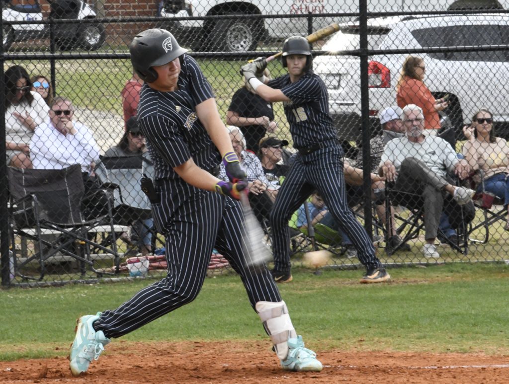 Baseball player in pinstripes hits the ball during a game, with another player on deck and spectators watching behind a fence.