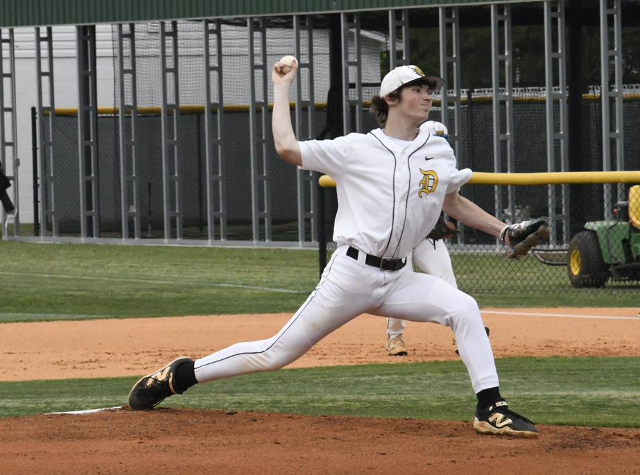 A baseball pitcher in a white uniform throws a pitch on a dirt mound during a game.