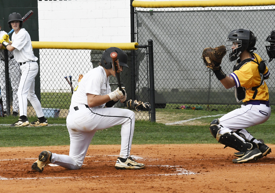 A baseball player kneels at home plate after being hit by a pitch while the catcher and an on-deck batter look on.