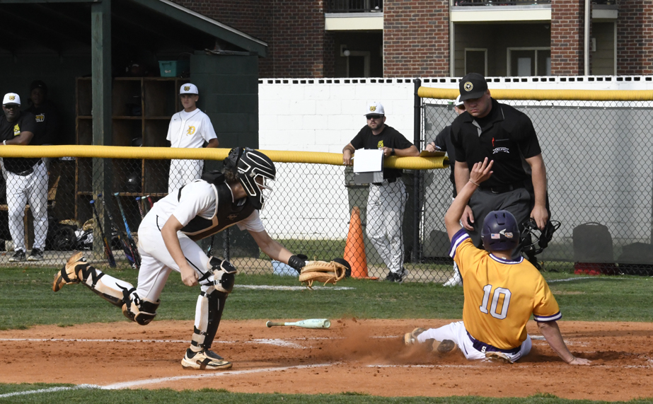 Baseball player in yellow sliding into home plate as catcher in white prepares to tag, with umpire and team members watching.